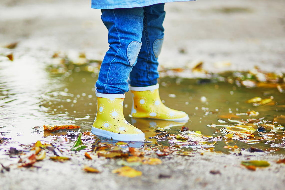 kid with rain boot standing in puddle